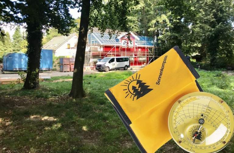 Sonnenkompass und im Hintergrund ein Holzhaus im Bau